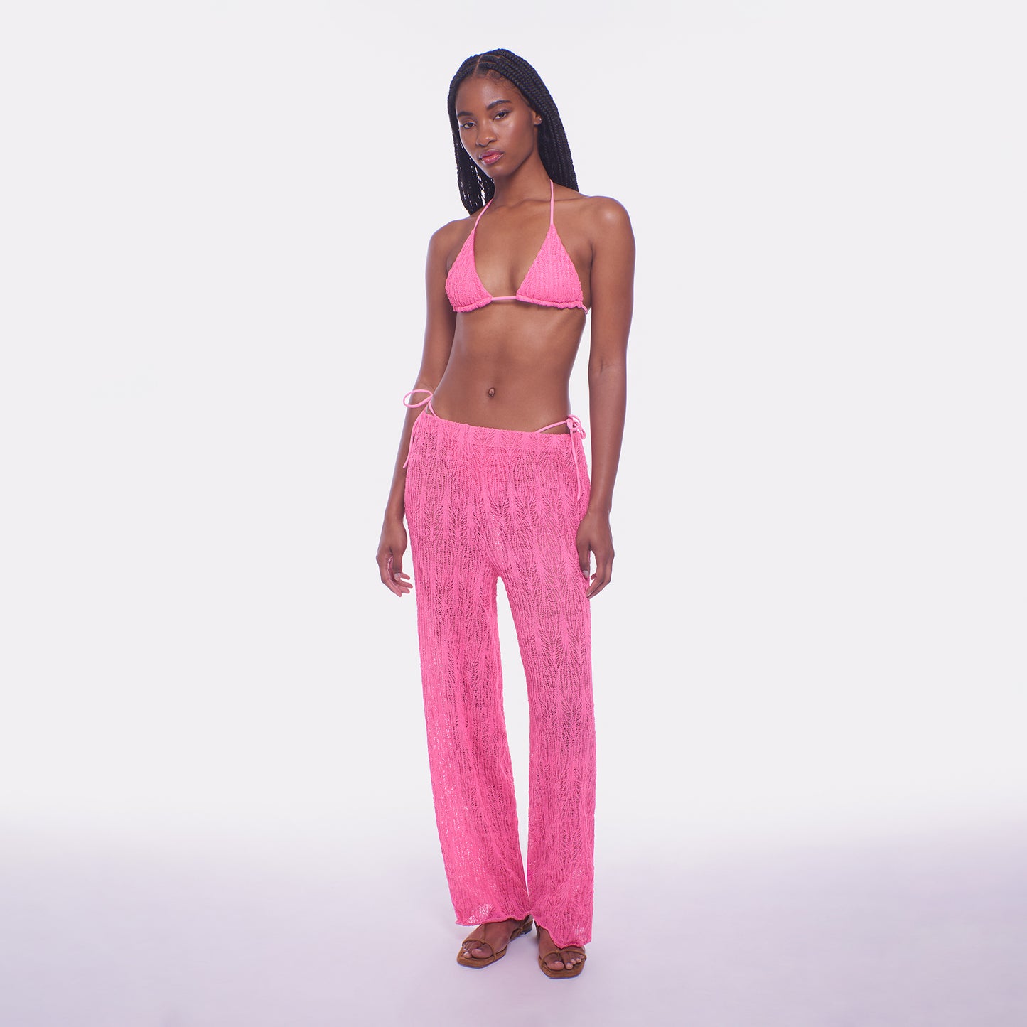 Woman wearing a pink bikini set with matching pants on a white background
