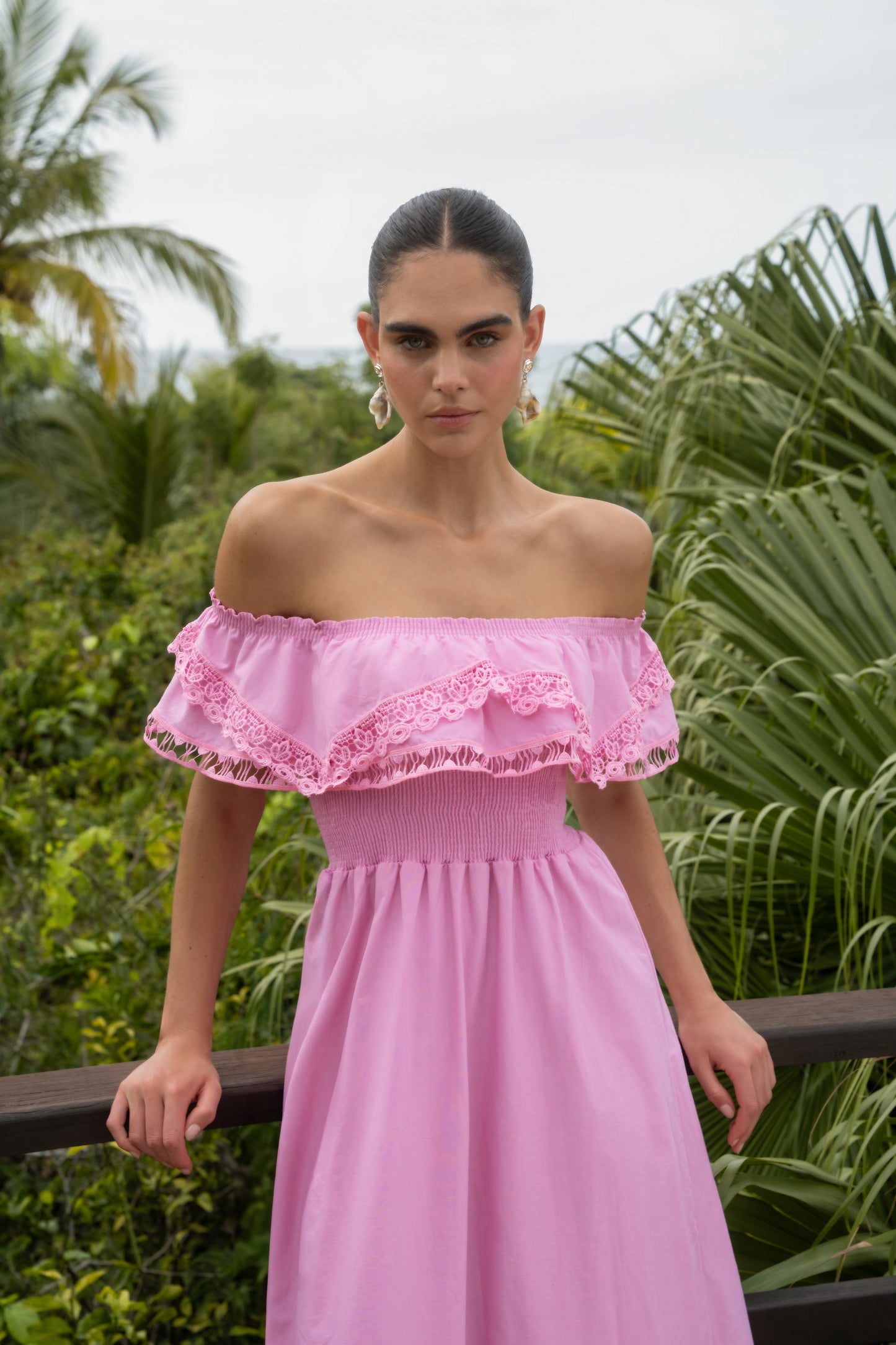 Woman wearing a pink off-shoulder dress with lace details in a tropical setting