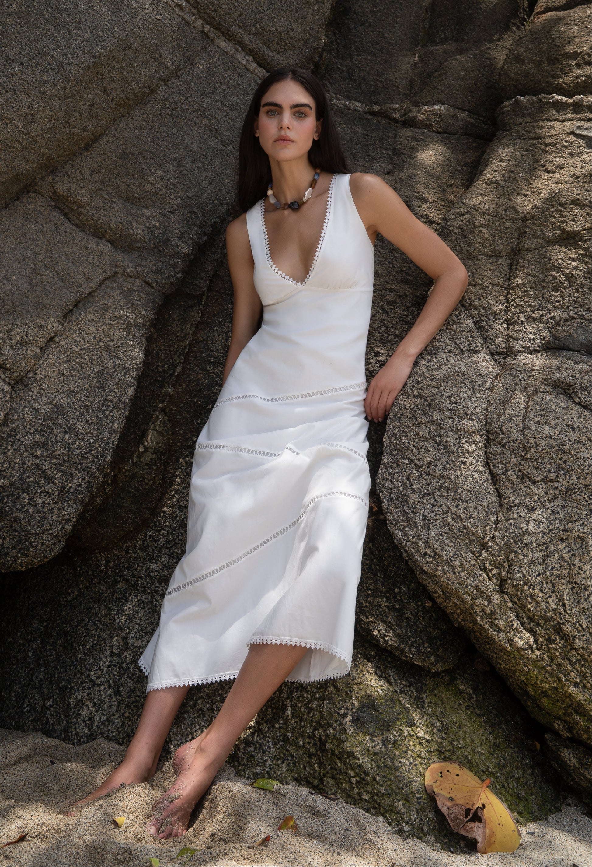 Woman in a white dress standing against large rocks on a beach