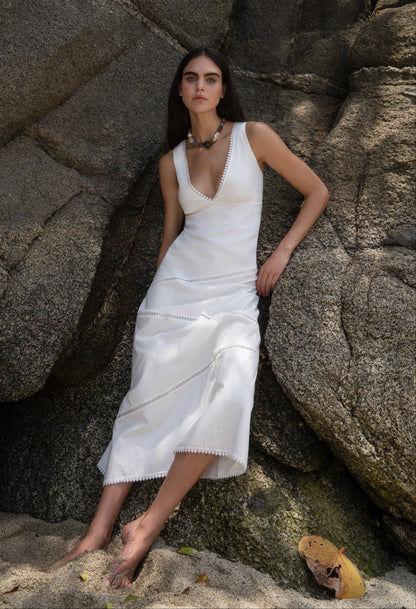 Woman in a white dress standing against large rocks on a beach