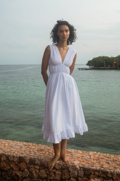 Woman in a white dress standing on a stone wall by a body of water.